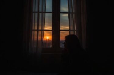 Persona orando en soledad junto a una ventana al atardecer