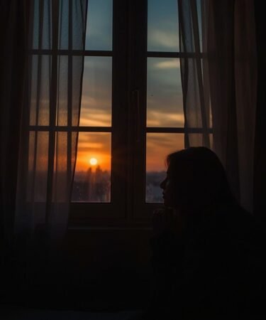 Persona orando en soledad junto a una ventana al atardecer